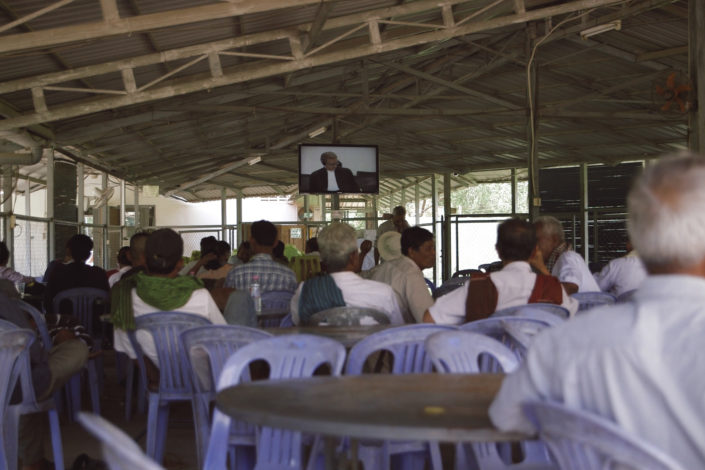 a room full of people watching a televised trial)