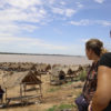 two female students look out over thatched roof huts towards the Mekong River