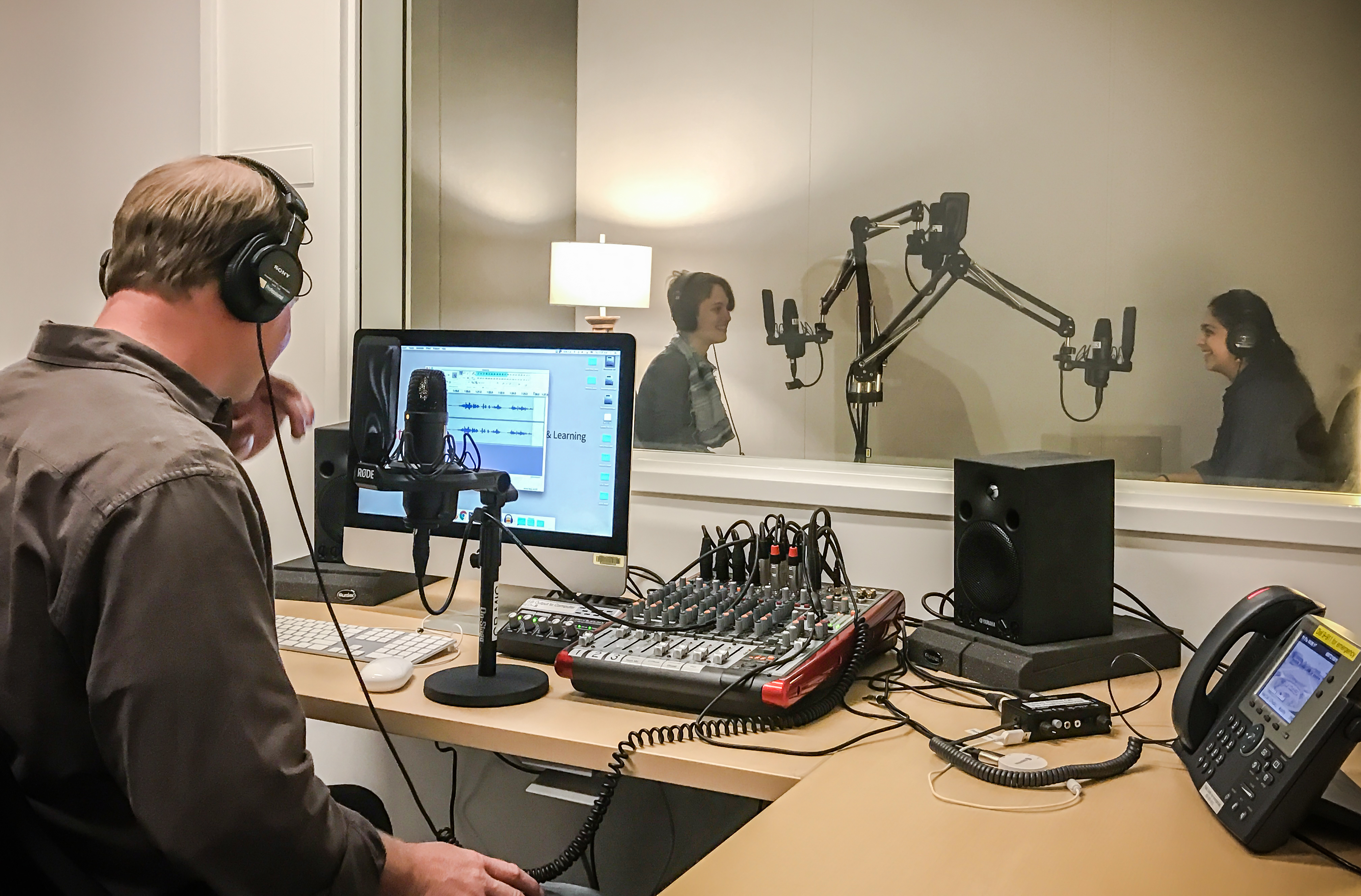 Michael Osborne, audio production director in a sound studio with students Megan Shea and Isha Salian practicing interview skills