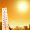 thermometer in foreground and city skyline in background under a blazing sun