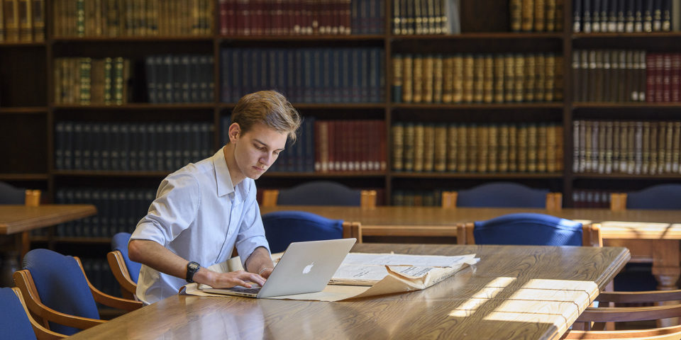 Undergraduate Anatole Schneider examing Italian newspapers from 1947-48 at the Hoover Library reading room.