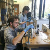 Professor Dustin Schroeder (foreground) and art historian Jessica Daniel splice 50-year-old film containing radar measurements of Antarctica into a reel in preparation for digital scanning at the Scott Polar Research Institute in the UK.