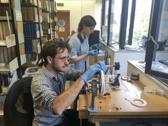 Professor Dustin Schroeder (foreground) and art historian Jessica Daniel splice 50-year-old film containing radar measurements of Antarctica into a reel in preparation for digital scanning at the Scott Polar Research Institute in the UK.