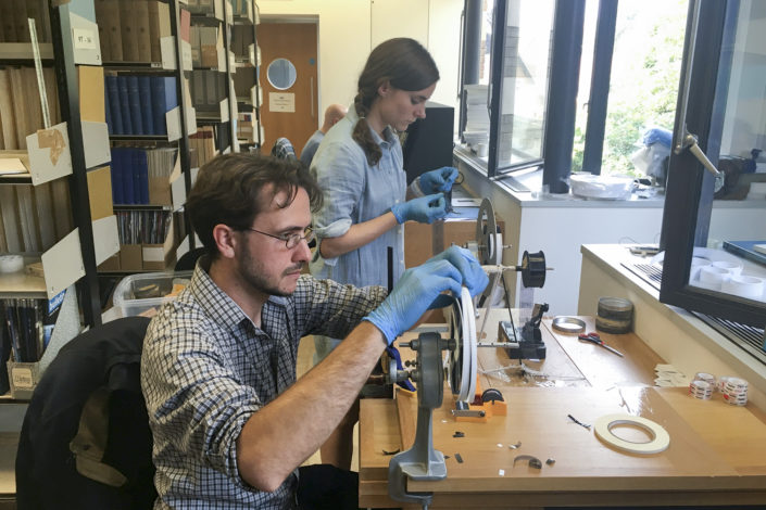 Professor Dustin Schroeder (foreground) and art historian Jessica Daniel splice 50-year-old film containing radar measurements of Antarctica into a reel in preparation for digital scanning at the Scott Polar Research Institute in the UK.)