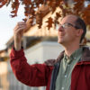 Alex Dunn stands under a tree and examines a leaf.