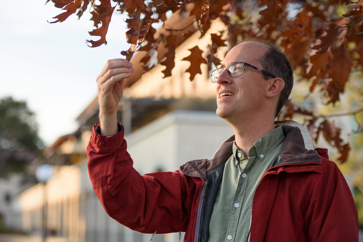 Alex Dunn stands under a tree and examines a leaf.