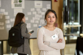 Emily Shaw standing with her arms crossed in front of a job board