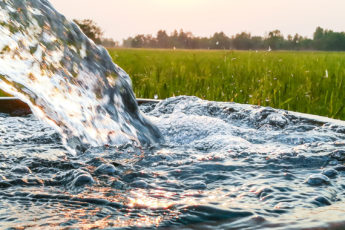 closeup of water pouring from an irrigation pipe with field in the background