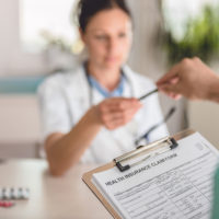 at the doctor's office, receptionist hands man a health insurance claim form