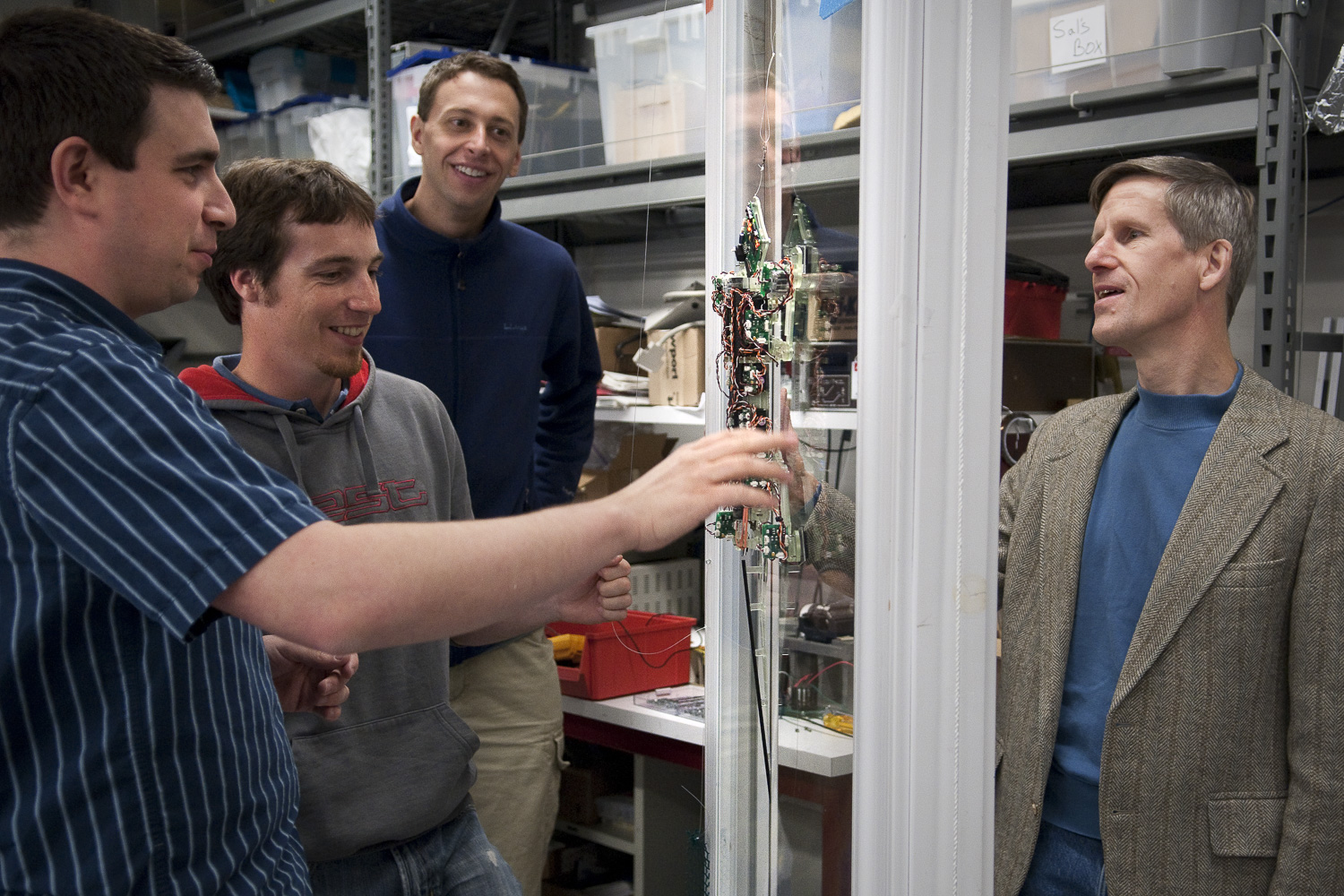 Four men watch Stickybot climb up a pane of glass