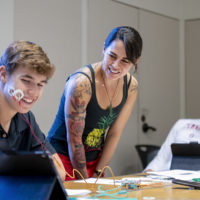 First-year Stanford student Karsten Householder observes the electrical impulses generated by his smile on an iPad – with the help of a pair of electrodes attached to his cheek – during a class meeting of “How Does Your Brain Work,” taught by Lecturer Lupita Ruiz-Jones, (center), who earned a PhD in marine biology at Stanford and is also an alumna of its Diversifying Academia, Recruiting Excellence Doctoral Fellowship Program.