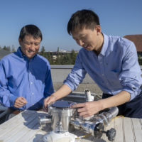 Professor Shanhui Fan and postdoctoral scholar Wei Li atop the Packard Electrical Engineering building with the apparatus that is proving the efficacy of a double-layered solar panel. The top layer uses the standard semiconductor materials that go into energy-harvesting solar cells, the novel materials on the bottom layer perform the cooling task.