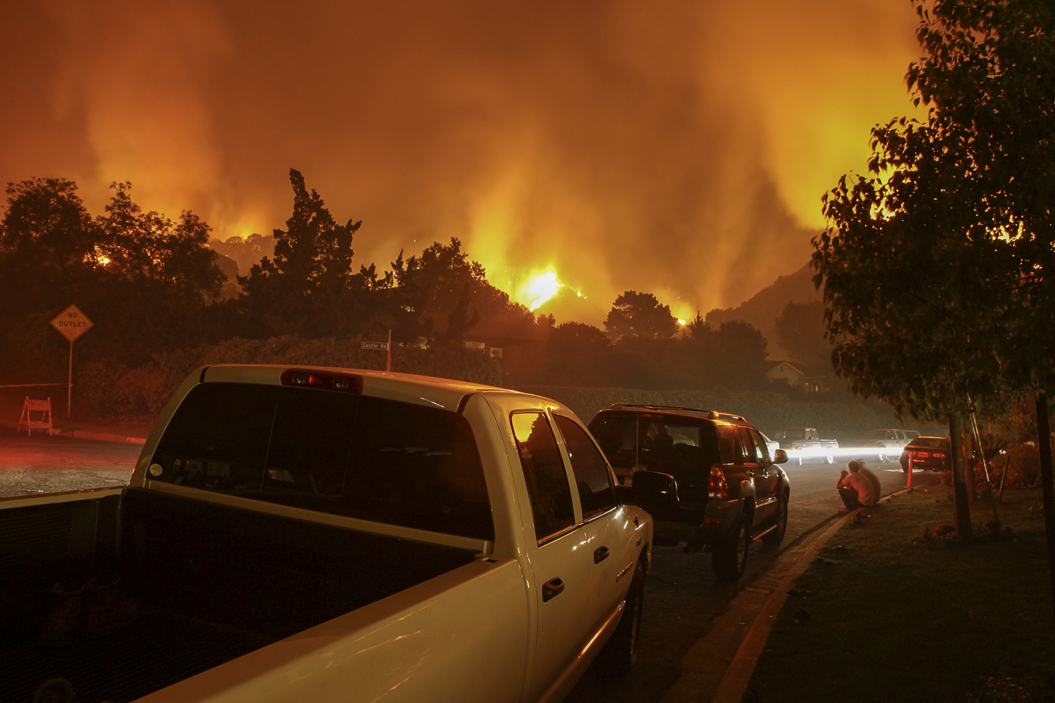 Residents of a neighborhood sit by and watch a fire threaten their homes.