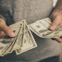 A man in a gray T-shirt holds dollars in his hands.