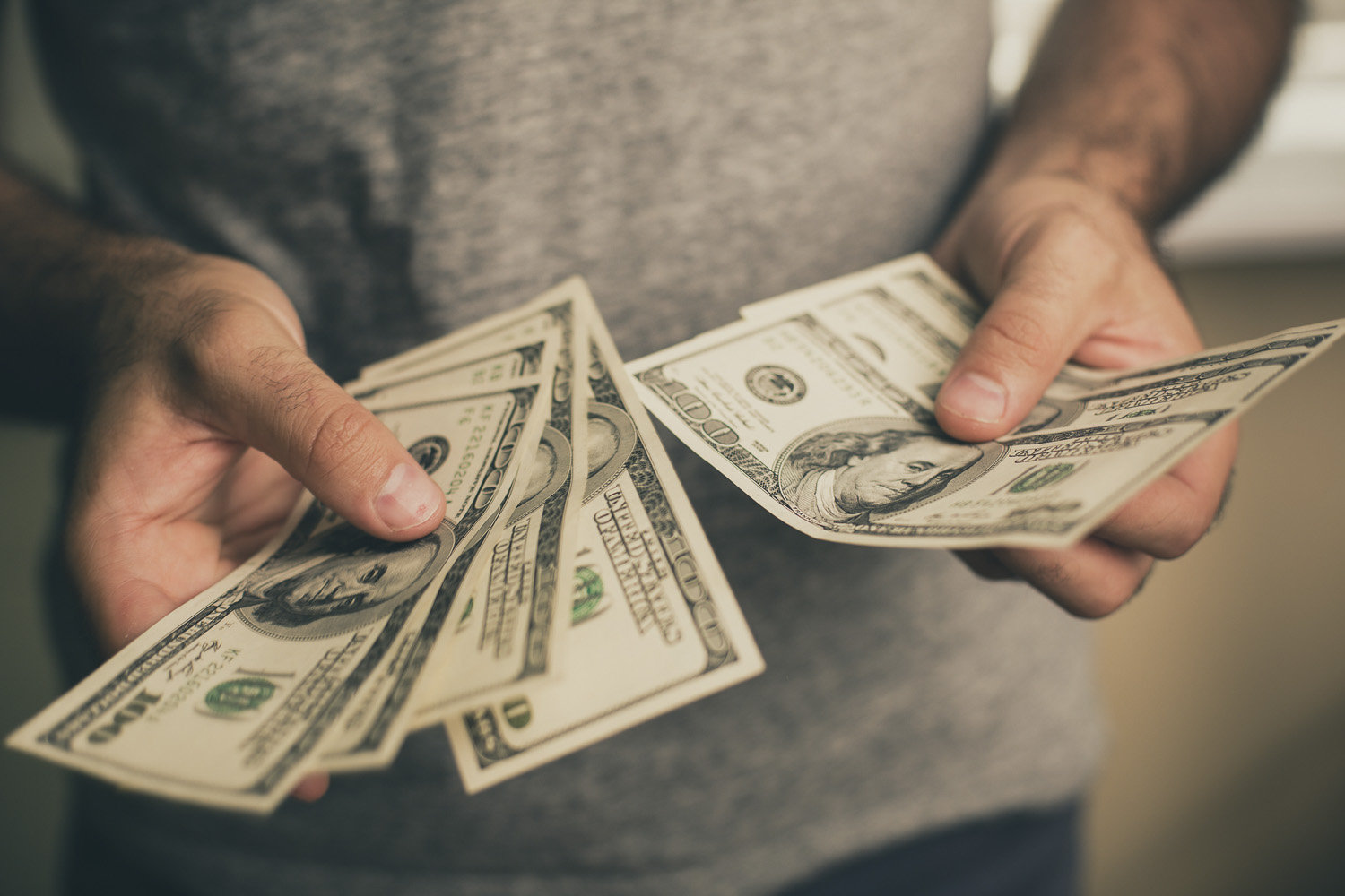 A man in a gray T-shirt holds dollars in his hands.