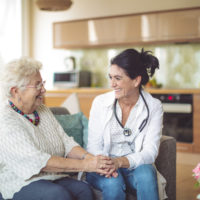 Doctor is sitting with a senior woman in a kitchen