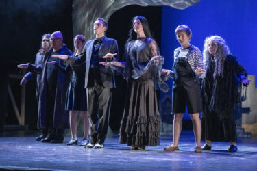 The seven members of the Addams Family sing.