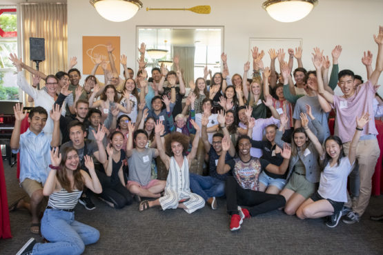 Students sitting on the floor with arms raised.