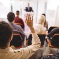 Rear view of a woman raising her hand to ask a question at a conference session.