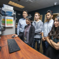 team of scientists standing, looking at a monitor