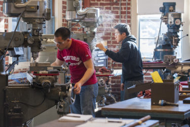 Two people working at band saws with other machines and tools around them