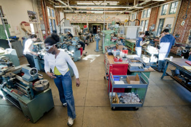 Several people working at different machines throughout a large room full of tools and equipment