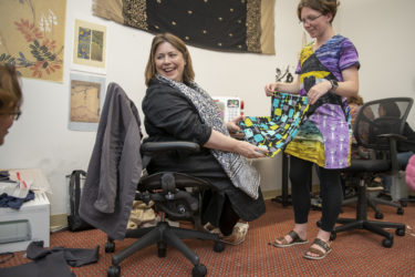 Two people hold a handmade shopping bag while smiling at someone off-camera