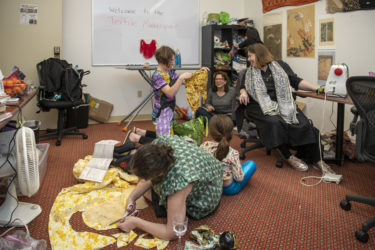 Five people in the room look at and work on sewing projects