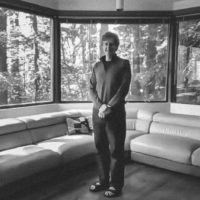 Chris Chafe standing in a room surrounded by windows with views of redwood trees