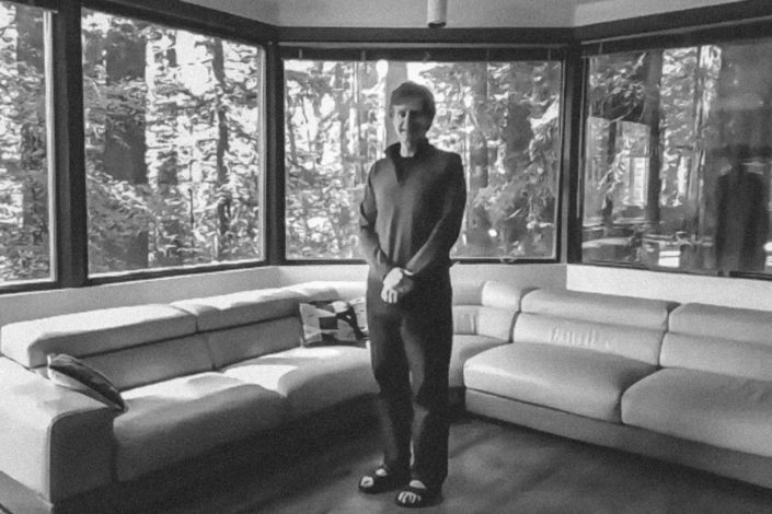 Chris Chafe standing in a room surrounded by windows with views of redwood trees