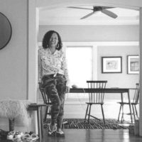 Debbie Seneksy smiling, leaning against a wall in-between a dining room and hallway