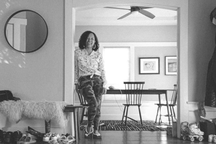 Debbie Seneksy smiling, leaning against a wall in-between a dining room and hallway