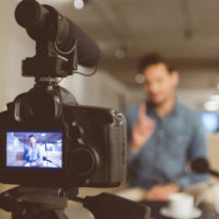 Male vlogger recording content for his video blog. Young man in focus on digital camera screen.