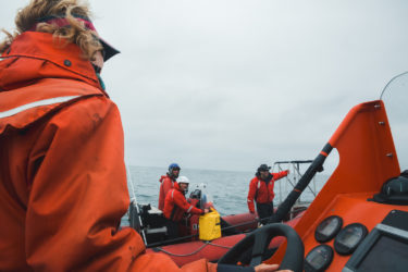 A person at the steering wheel of one boat talks with three people on another boat