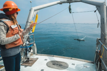 Person holding a line attached to a net that's trailing in the water behind the boat