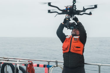 Person wearing a helmet and glasses holding a drone over his head