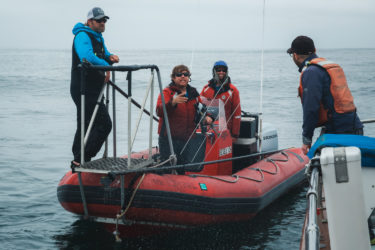 Three people on a boat talk with another person on a different boat