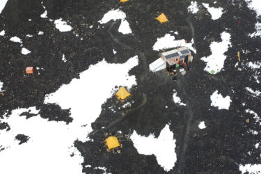 View from above with four pyramid-shaped tents and a small, rectangular building on black ground with some snow