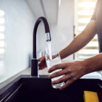 Close up of young man pouring fresh water from kitchen sink.