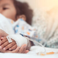 Hand holding child's hand in hospital bed