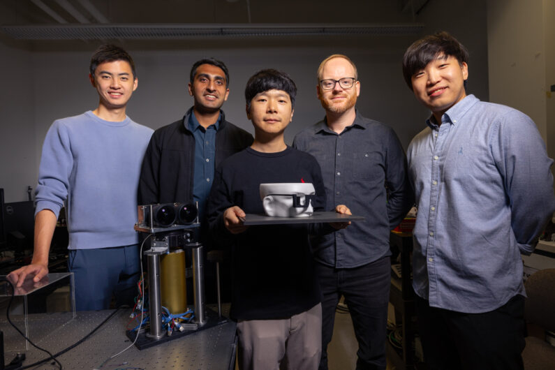 Five people standing and facing the camera. The person in the middle is holding a mannequin head with protoype glasses.